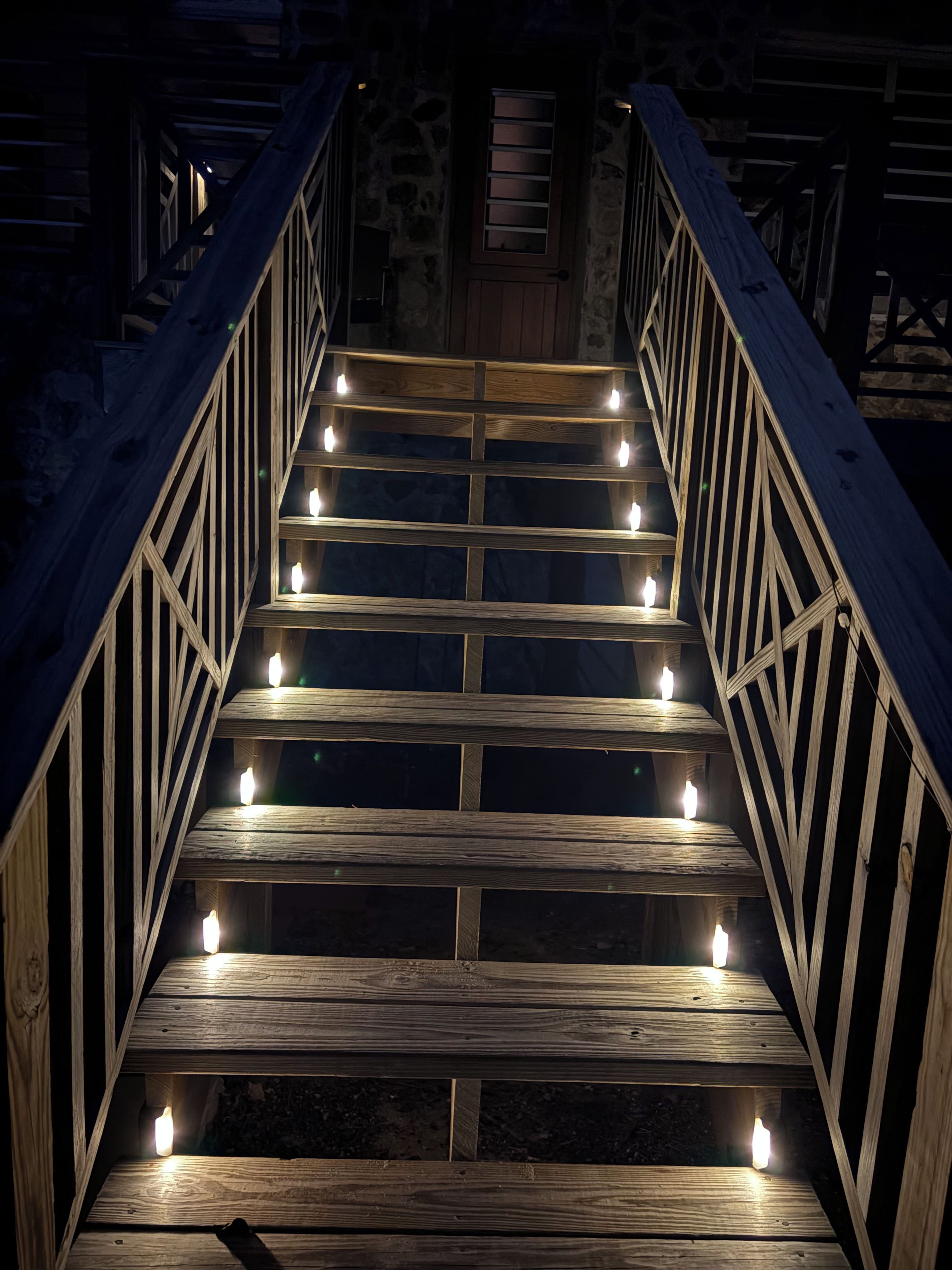 A wooden staircase with evenly spaced steps and handrails on both sides, leading to a door with a window.