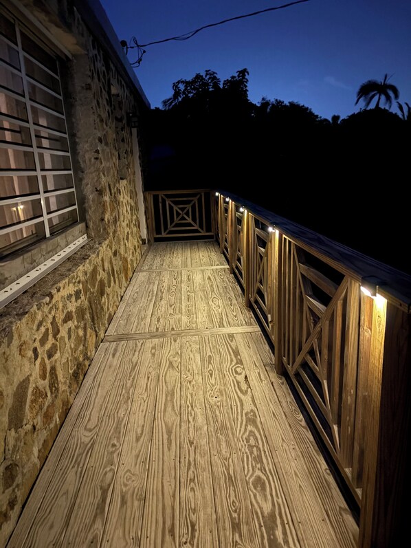 Een houten terras met aan één kant een stenen muur en aan de andere kant een houten balustrade, verlicht met lichtslingers.
