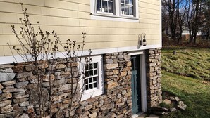 Une maison avec des fondations en pierre, un petit porche à l’avant et une fenêtre à cadre blanc.