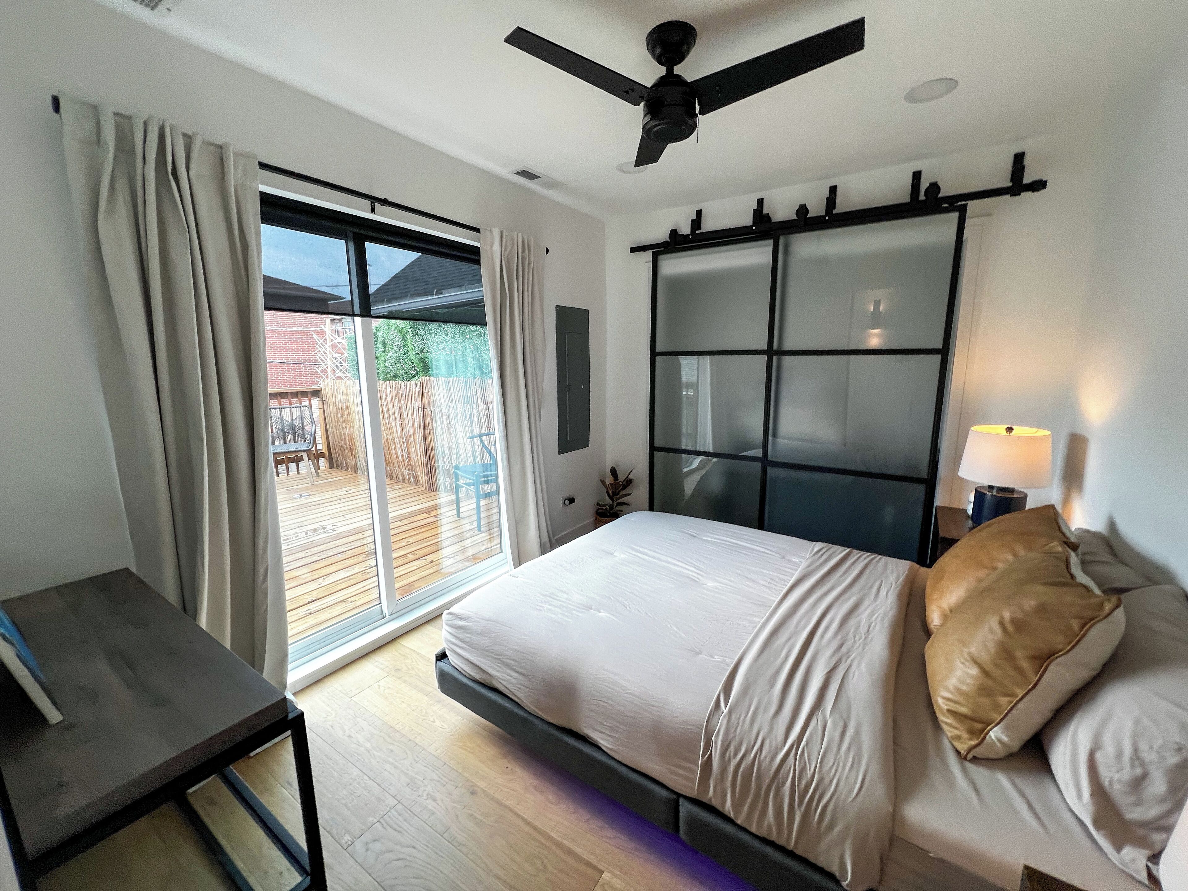 A bedroom with a bed, a desk, and a sliding glass door to a patio.