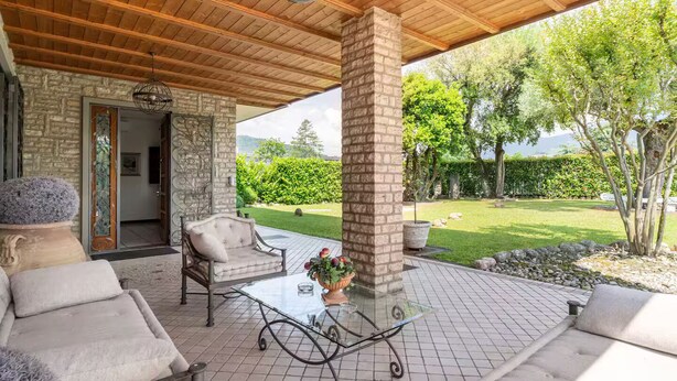 Un patio al aire libre con un muro de piedra, techo de madera y mesa de vidrio.
