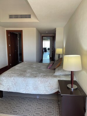 A hotel room with a large bed, a bedside table with a lamp, a door, and a view of the balcony. - Beachfront in Puerto Vallarta | Spectacular view + pool + beach access (Puerto Vallarta)