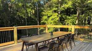 A wooden deck with a table and chairs, surrounded by a metal railing and trees.