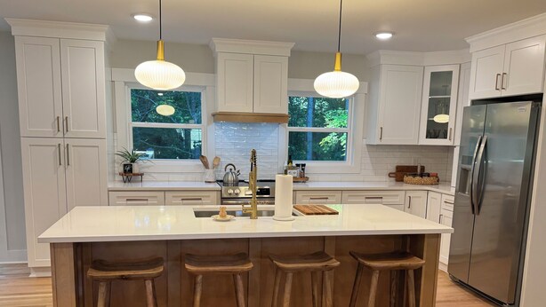 A modern kitchen with white cabinets, a large island with stools, stainless steel appliances, and pendant lighting.