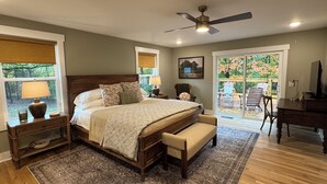 A bedroom with a large bed, a ceiling fan, a desk, and a view of the outdoors.