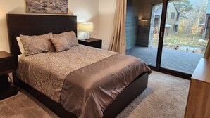 Une chambre avec un grand lit, une table de chevet avec une lampe, un tableau représentant un paysage désertique et une vue sur une terrasse et l’espace extérieur.