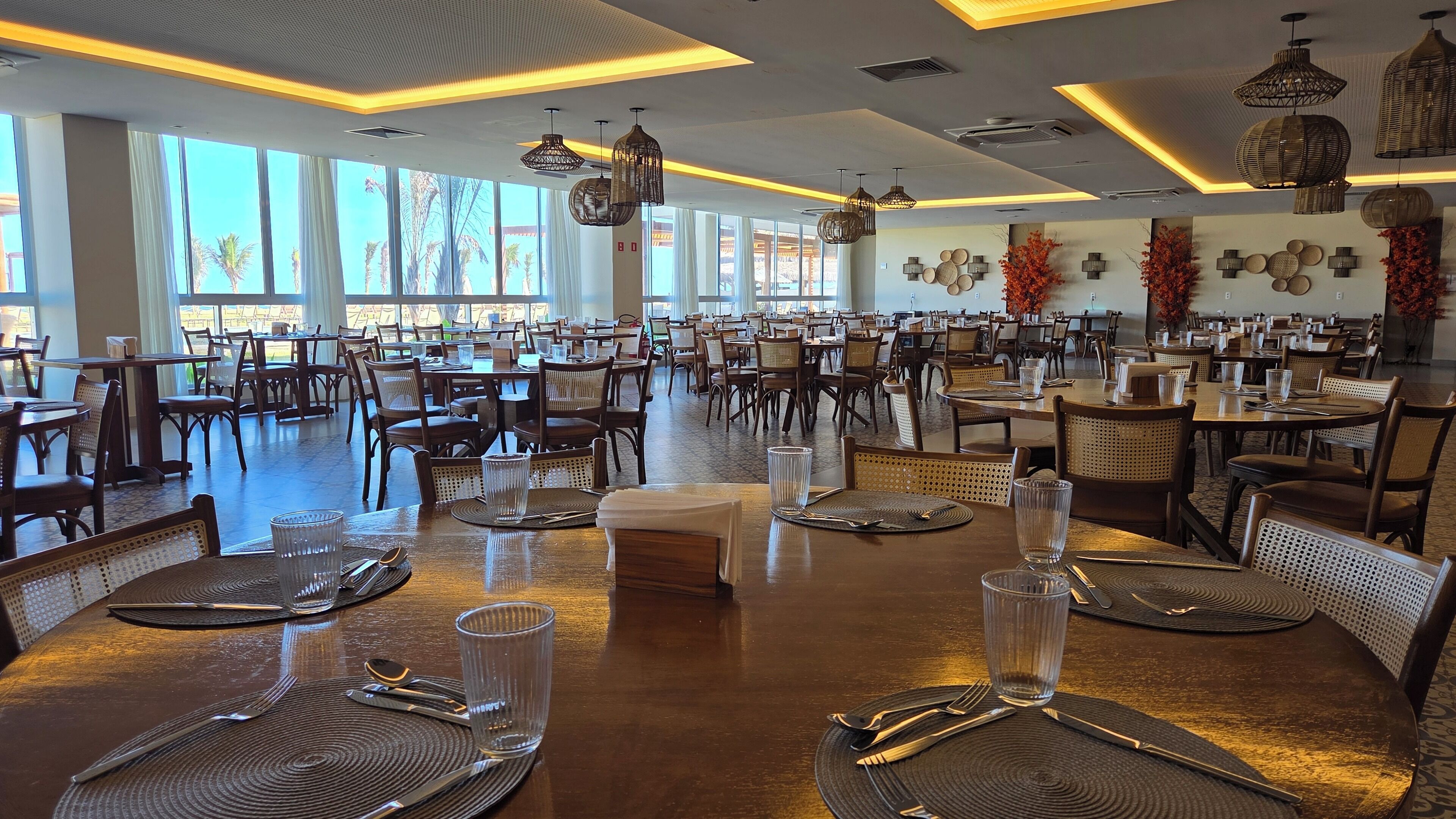 A spacious dining area with multiple tables set for dining, large windows allowing natural light, and modern lighting fixtures.