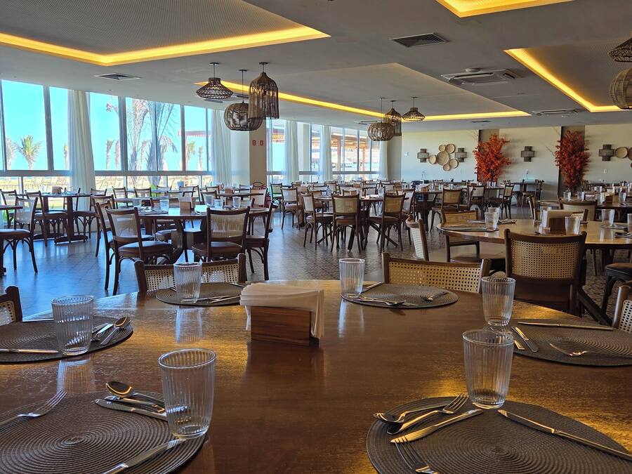 A spacious dining area with multiple tables set for dining, large windows allowing natural light, and modern lighting fixtures.