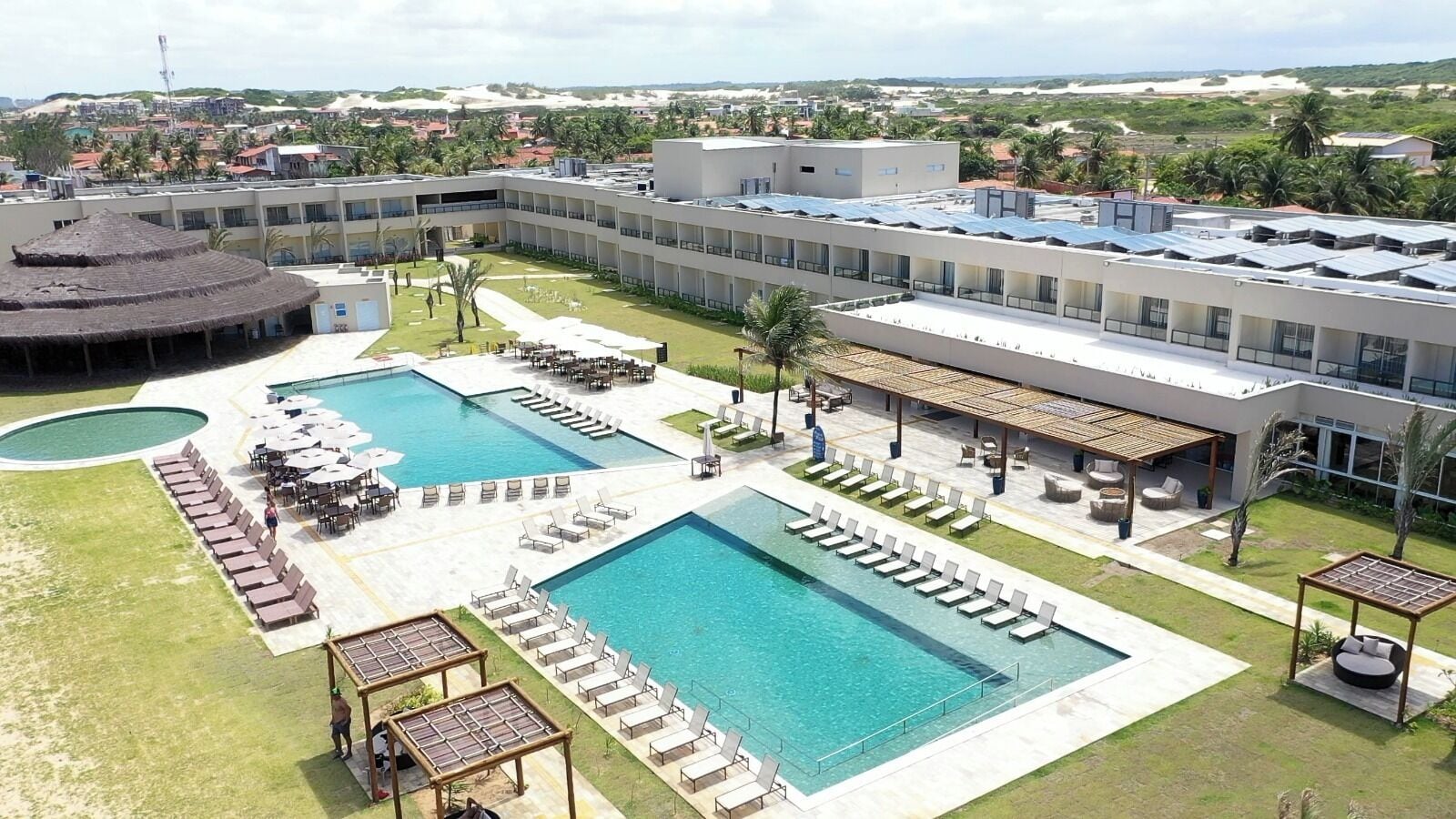 A resort with two large swimming pools, sun loungers, and outdoor seating areas.