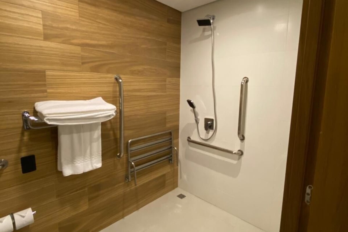 A modern bathroom with a wooden wall, a sink, a shower, and a towel rack.