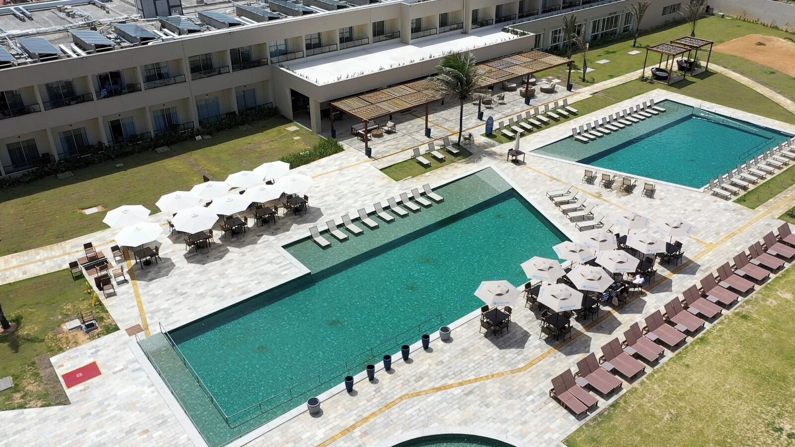 A hotel with a large outdoor pool area, multiple lounge chairs, and umbrellas.