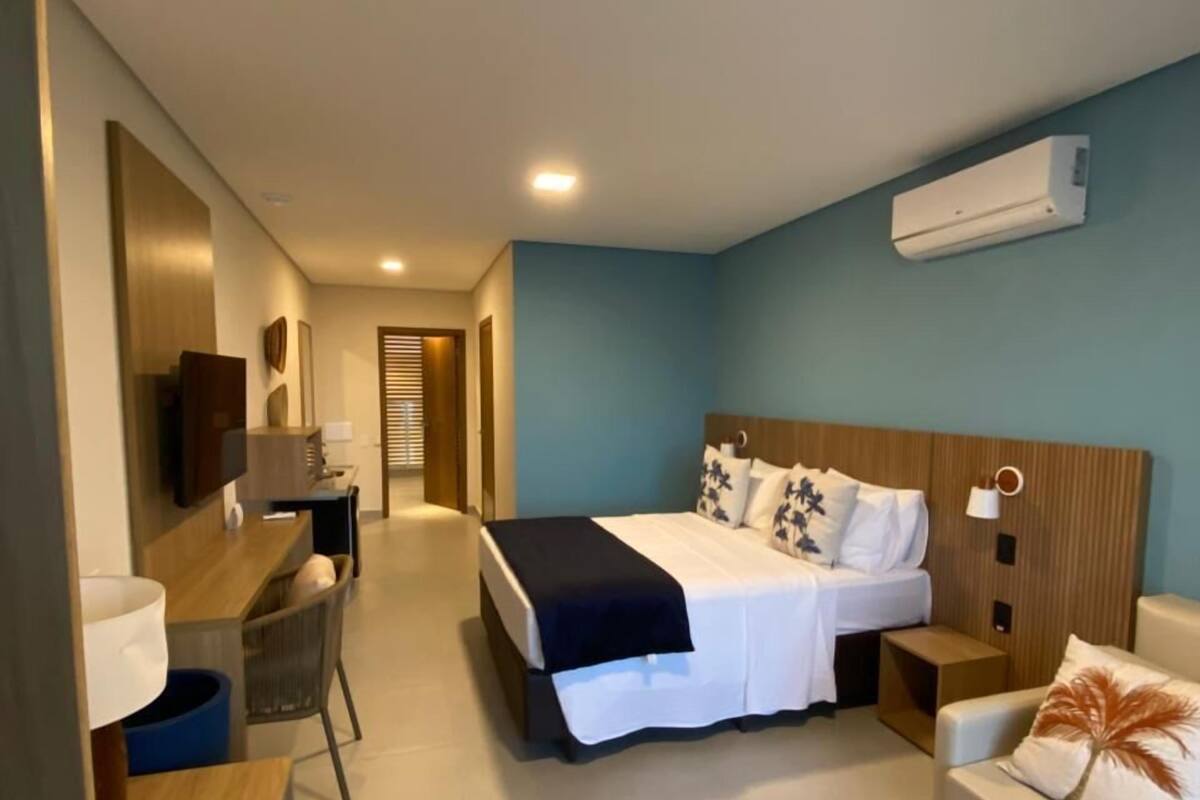 A modern hotel room with a bed, a desk, a chair, a sofa, and an air conditioning unit.
