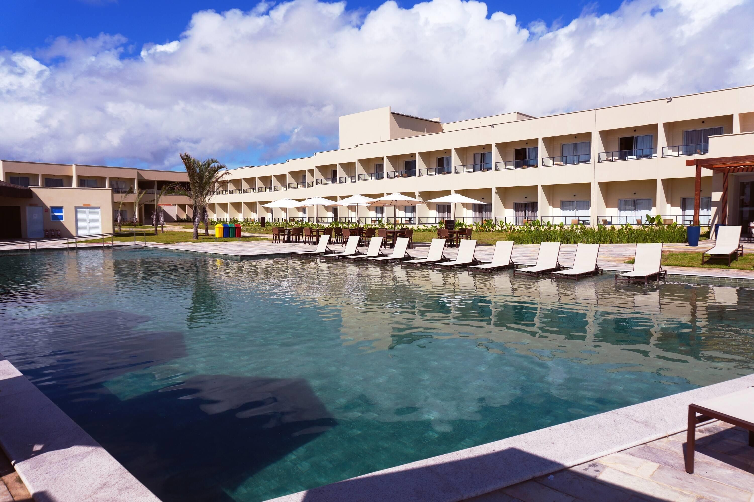 A hotel with a swimming pool, lounge chairs, and a covered seating area.