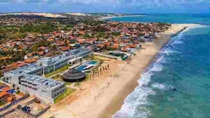 Vista aérea de un complejo turístico costero con playa, un gran edificio de hotel y una zona de piscina.