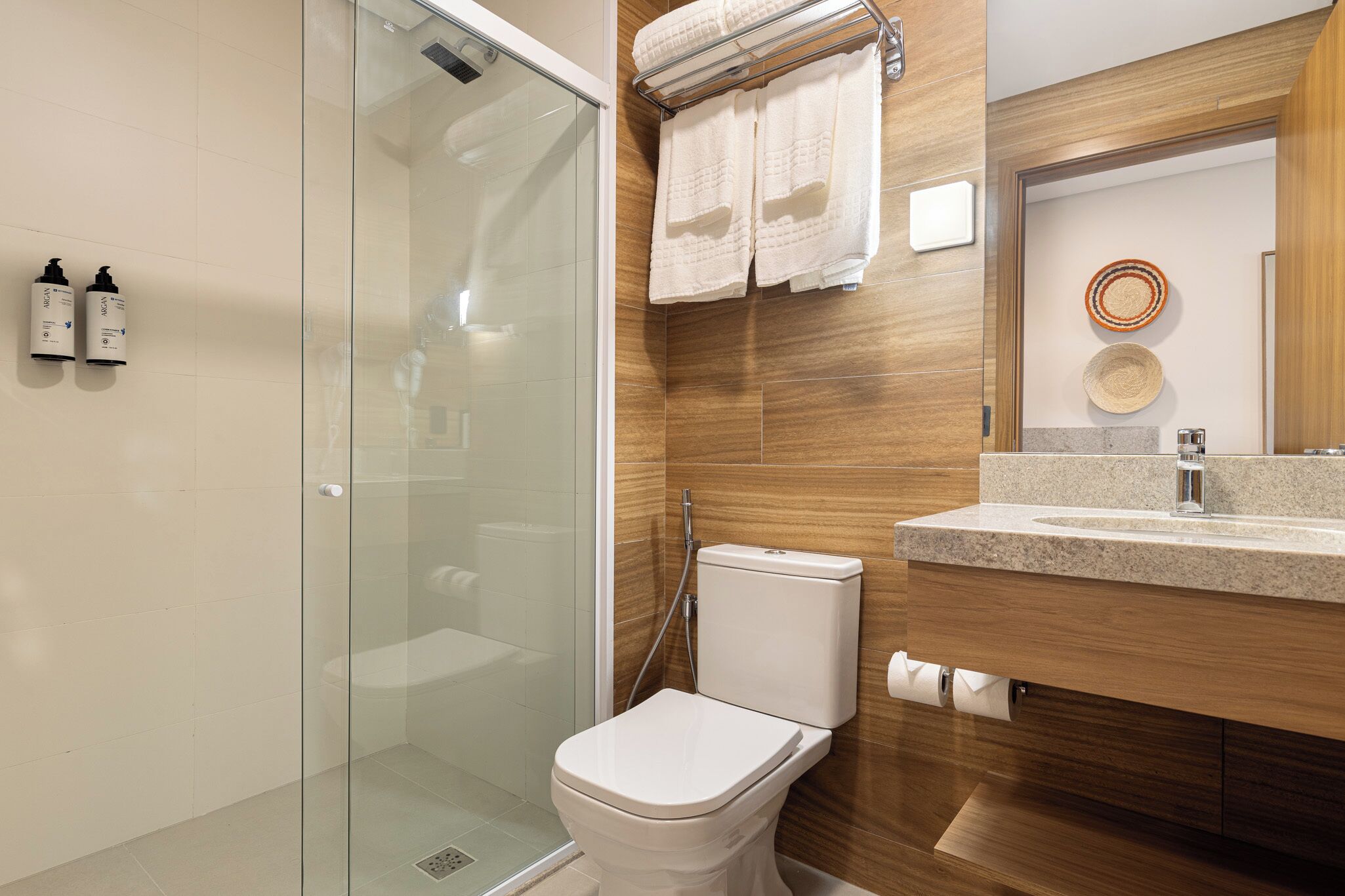 A modern bathroom with a glass shower enclosure, a white toilet, a wooden vanity with a sink, and two wall-mounted towel racks.
