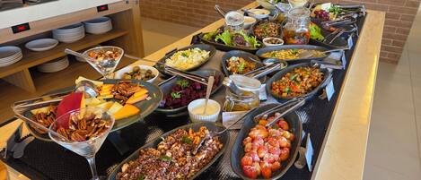 A buffet with various dishes including quinoa salad, roasted vegetables, and a selection of cheeses.