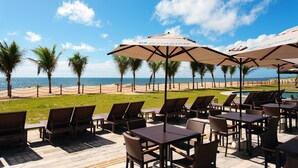 Un patio frente a la playa con mobiliario exterior, sombrillas y vistas al océano.