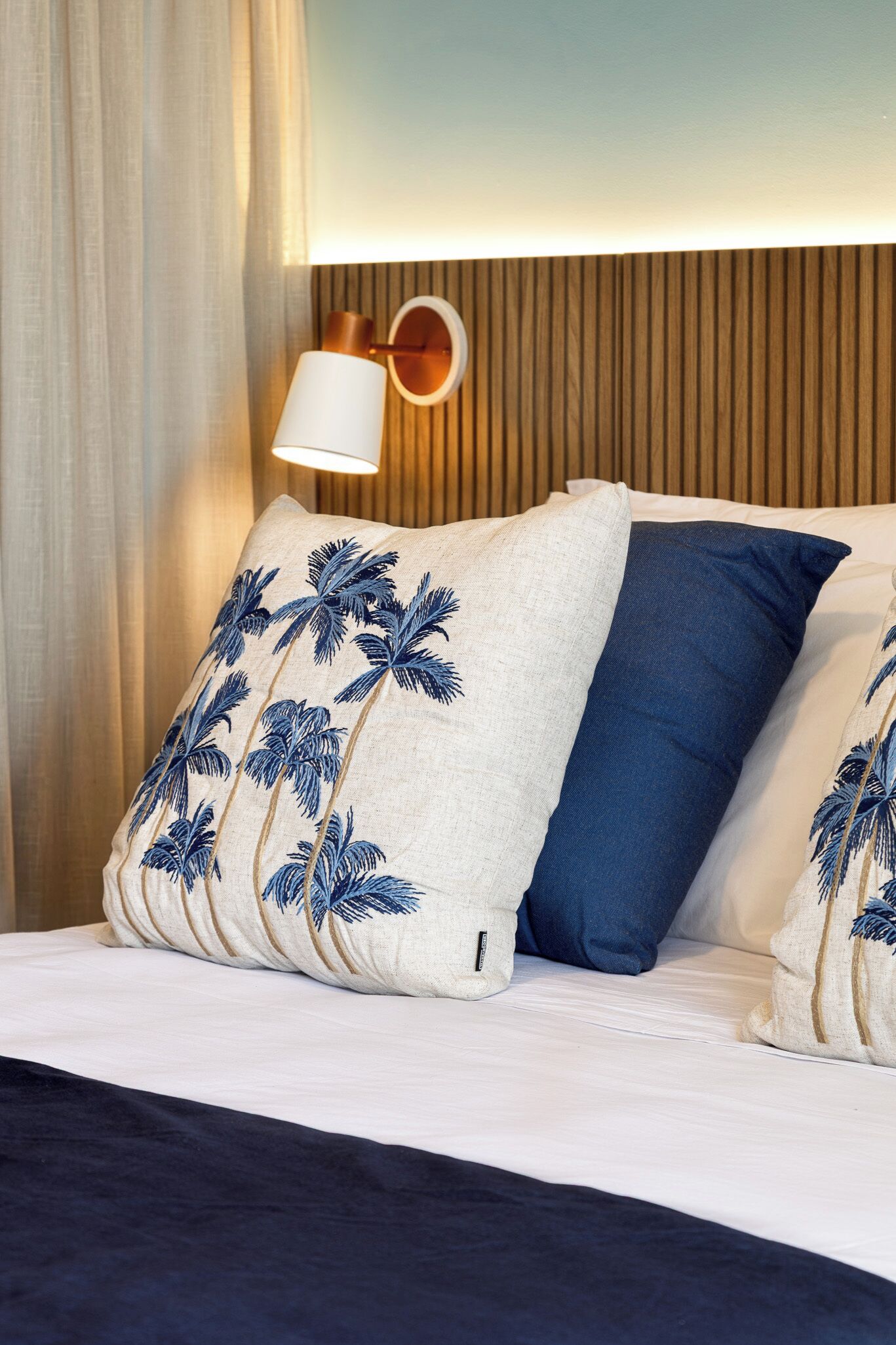 A bed with white and blue pillows, a wooden headboard, and a wall-mounted lamp.