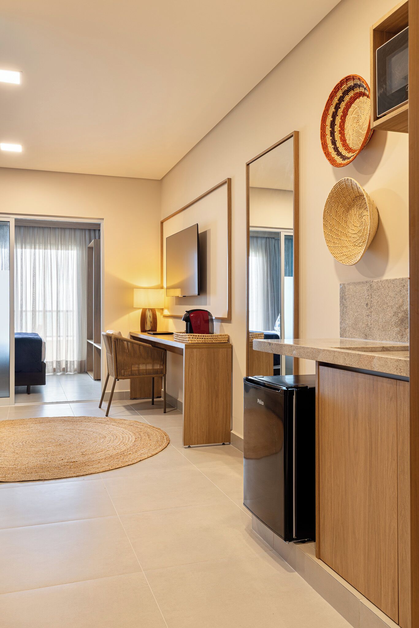 Una habitación de hotel moderna con kitchenette, zona de comedor y un espejo grande.