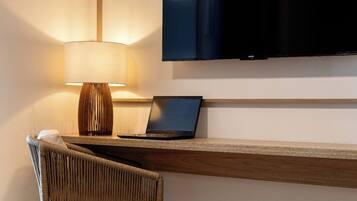 Quarto moderno com televisão de tela plana na parede, um laptop sobre uma escrivaninha de madeira, uma cadeira de vime e um abajur.