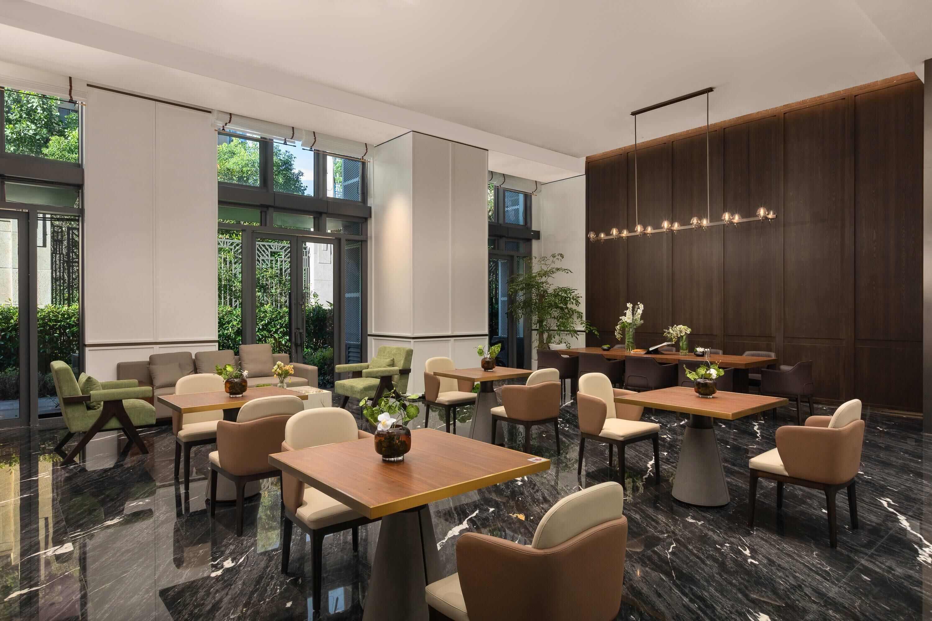 A modern dining area with tables and chairs, large windows, and a chandelier.
