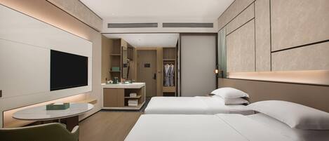 Una habitación de hotel moderna con televisor de pantalla plana, una mesita redonda, dos camas, una silla verde, un baño con espejo y un armario con ropa colgada.