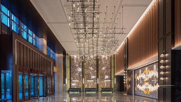 Um lobby moderno com piso de mármore refletivo, luminária central e uma parede grande com textura.