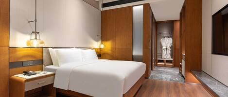 Ein modernes Hotelzimmer mit einem großen Bett, Holzvertäfelung, einem Schreibtisch mit Telefon und einem Bademantel im Flur.