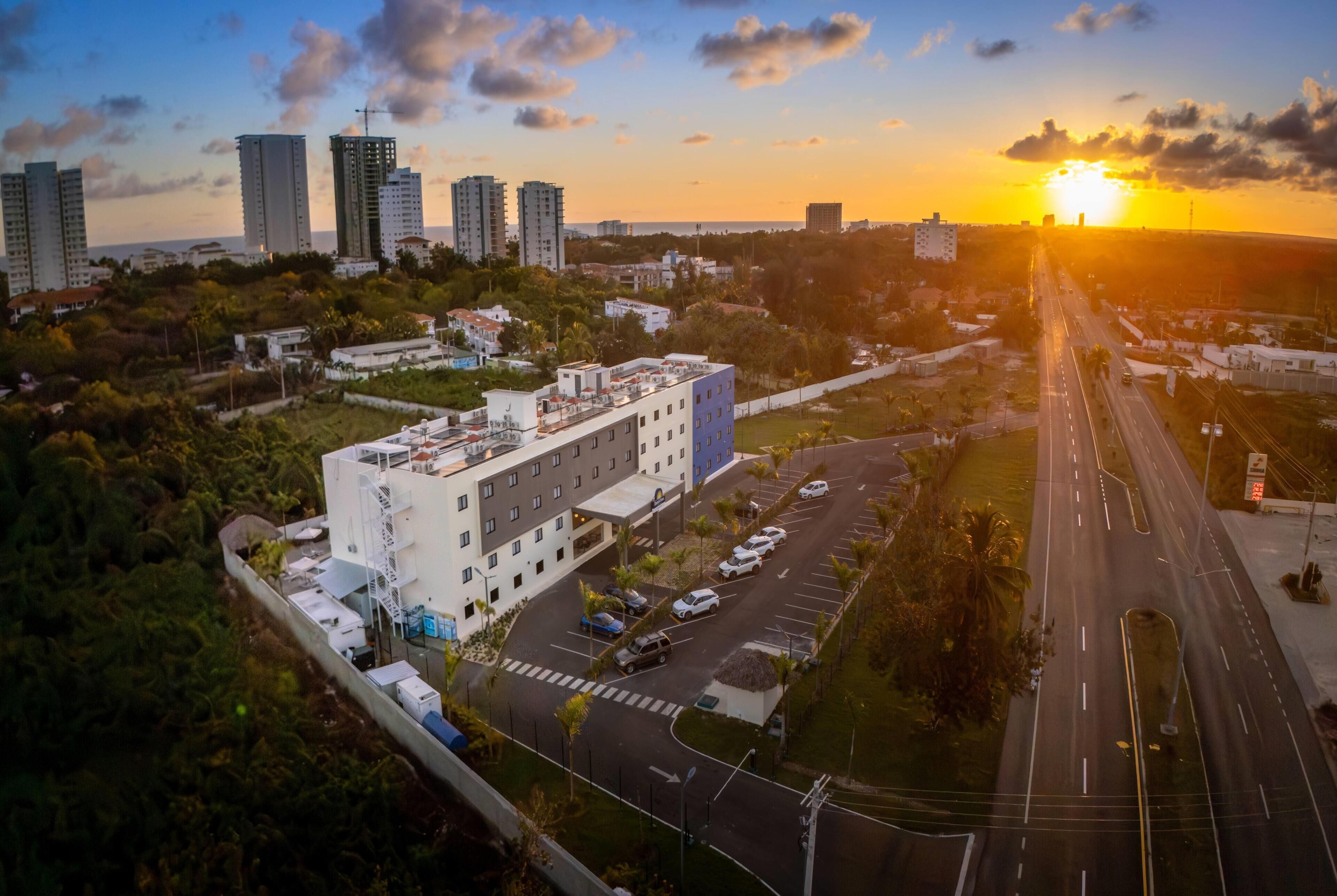 An aerial view of a cityscape with a prominent building, a road, and surrounding greenery.