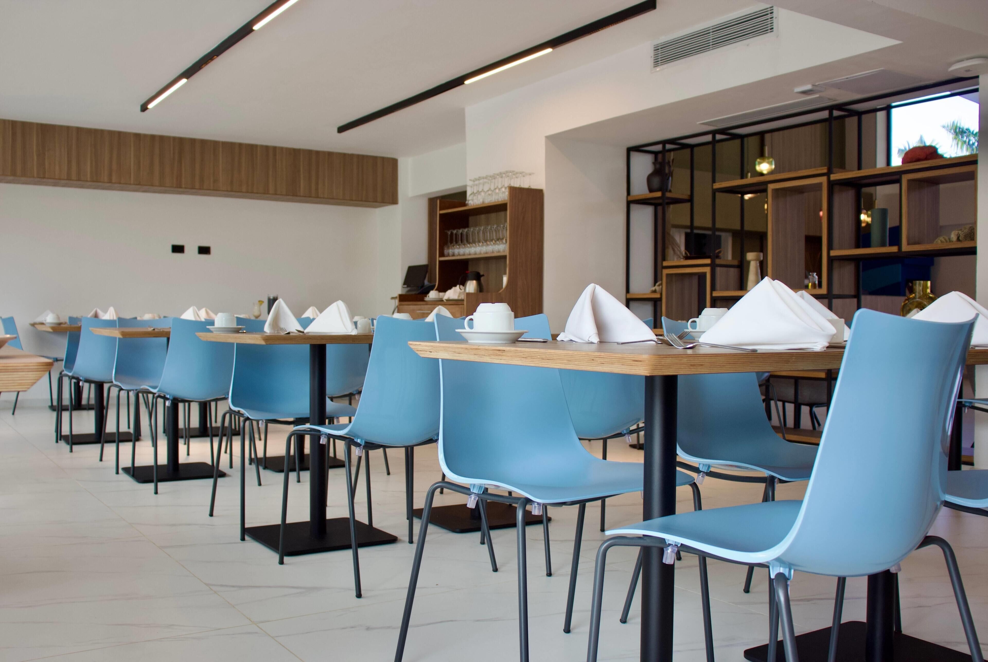 A modern dining area with blue chairs, wooden tables, and a kitchen in the background.