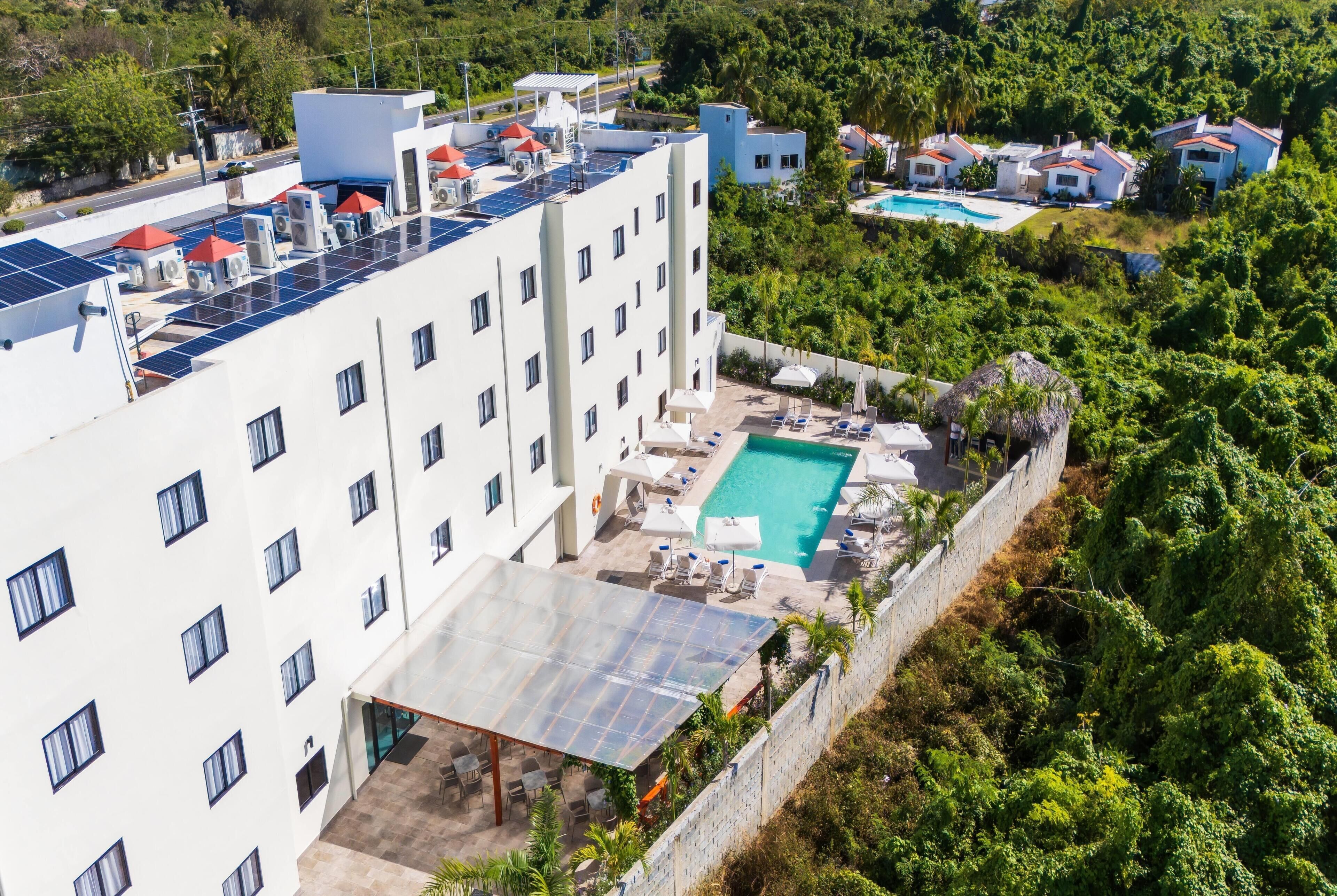 A hotel with a rooftop pool, solar panels, and a lush green environment.
