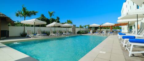 A swimming pool with lounge chairs and umbrellas, surrounded by palm trees and a clear blue sky.