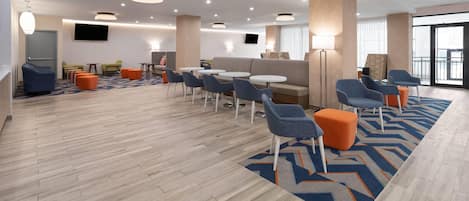 A modern hotel lobby with a mix of seating options, including sofas, chairs, and round tables.