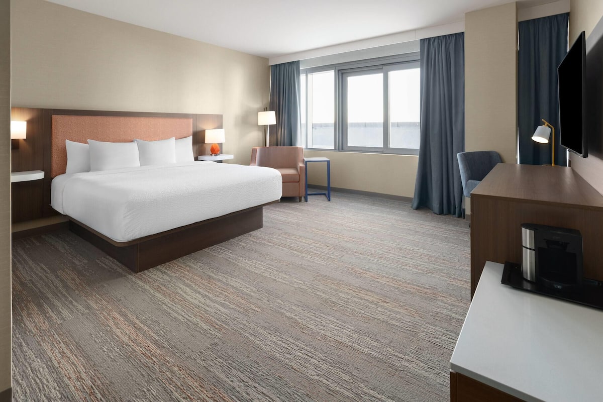 Une chambre d’hôtel avec un grand lit, un bureau, une chaise, une télévision et une fenêtre avec des rideaux.