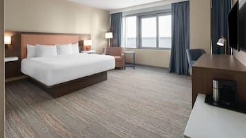 A hotel room with a large bed, a desk, a chair, a TV, and a window with curtains.