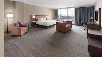 A hotel room with a large bed, two armchairs, a desk, and a TV.