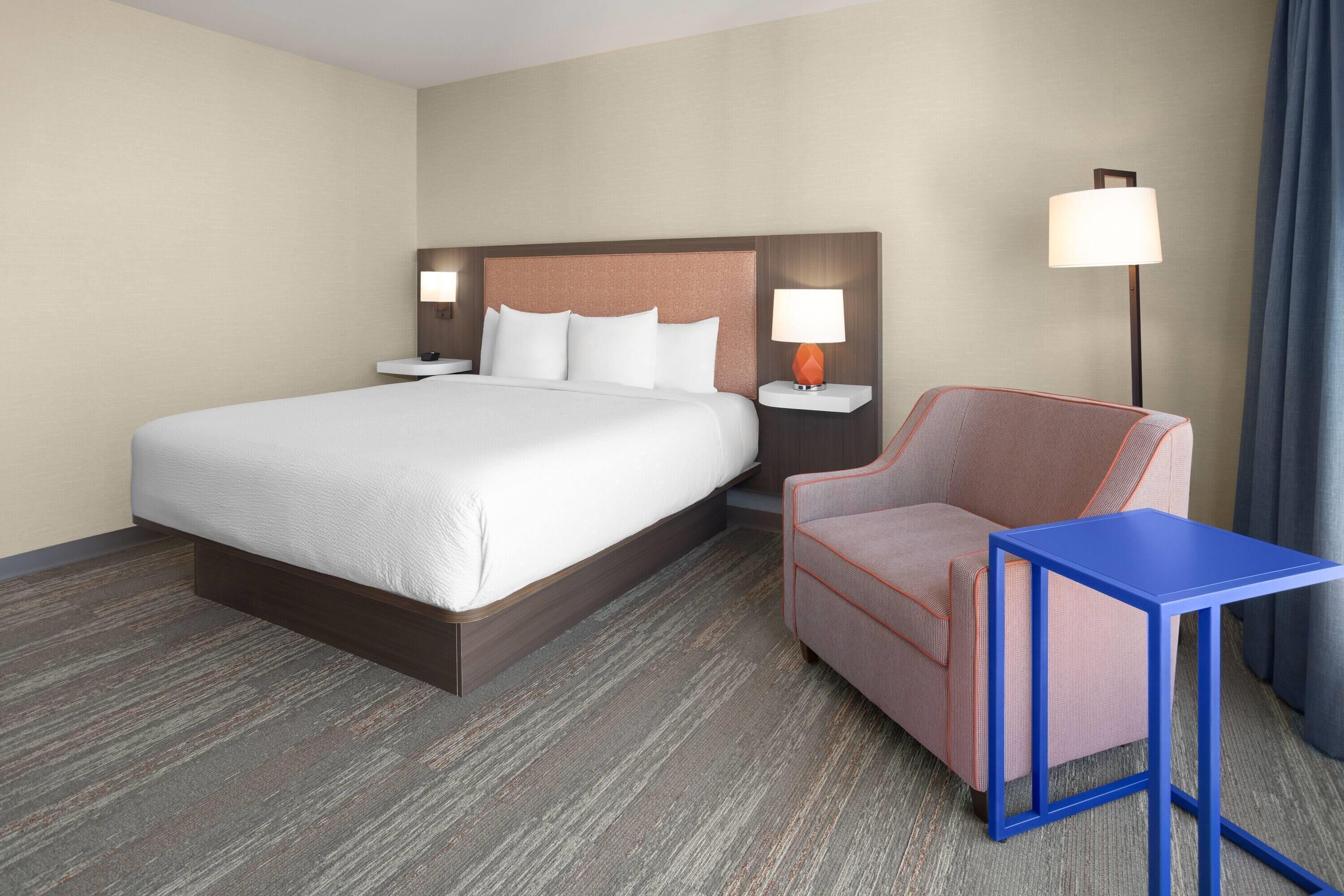 A hotel room with a large bed, a chair, a small table, and two bedside lamps.