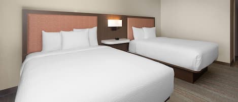 Una habitación de hotel con dos camas, una mesita de noche y una lámpara de pared.