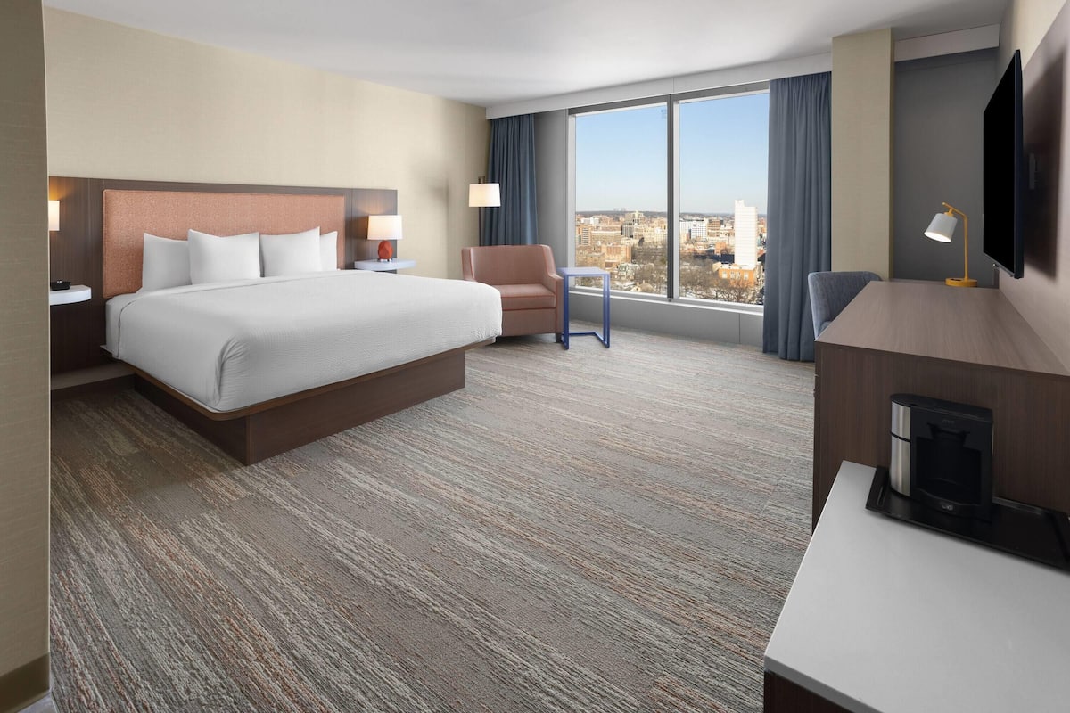 Une chambre d’hôtel avec un grand lit, un bureau, une chaise, une télévision et une vue sur la ville.