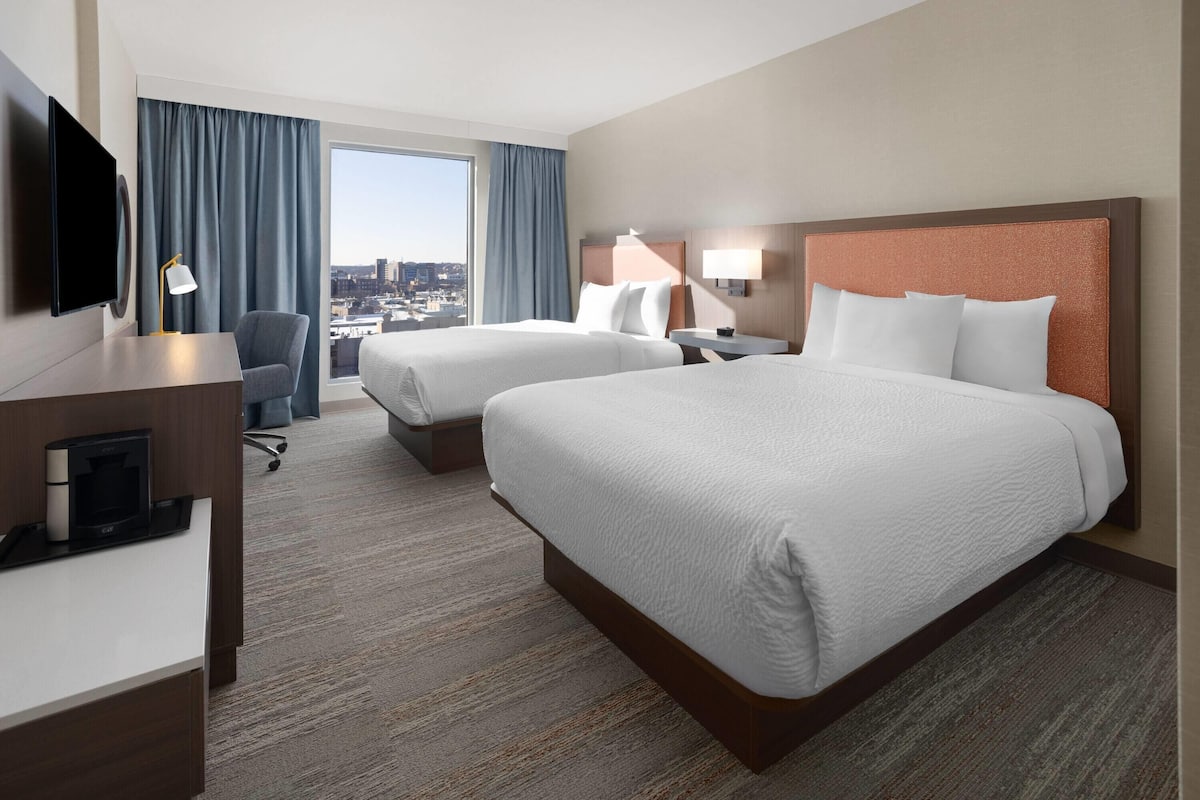 Une chambre d’hôtel avec deux lits, un bureau, une télévision et une vue sur la ville.