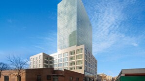 A modern high-rise building with a glass facade, surrounded by other buildings. - La Quinta Inn & Suites By Wyndham Queens NYC/JFK AirTrain (Jamaica)