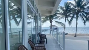 Ein überdachter Balkon mit Korbstühlen, Glastüren und Blick auf das Meer und Palmen.