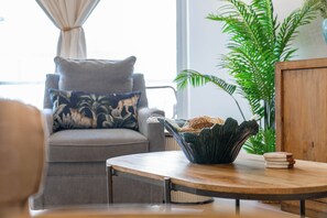 A modern living room with a grey sofa, a wooden coffee table, and a green plant. - Styles Beach 1B - Beach View Condo w/ Pool (San Pedro)