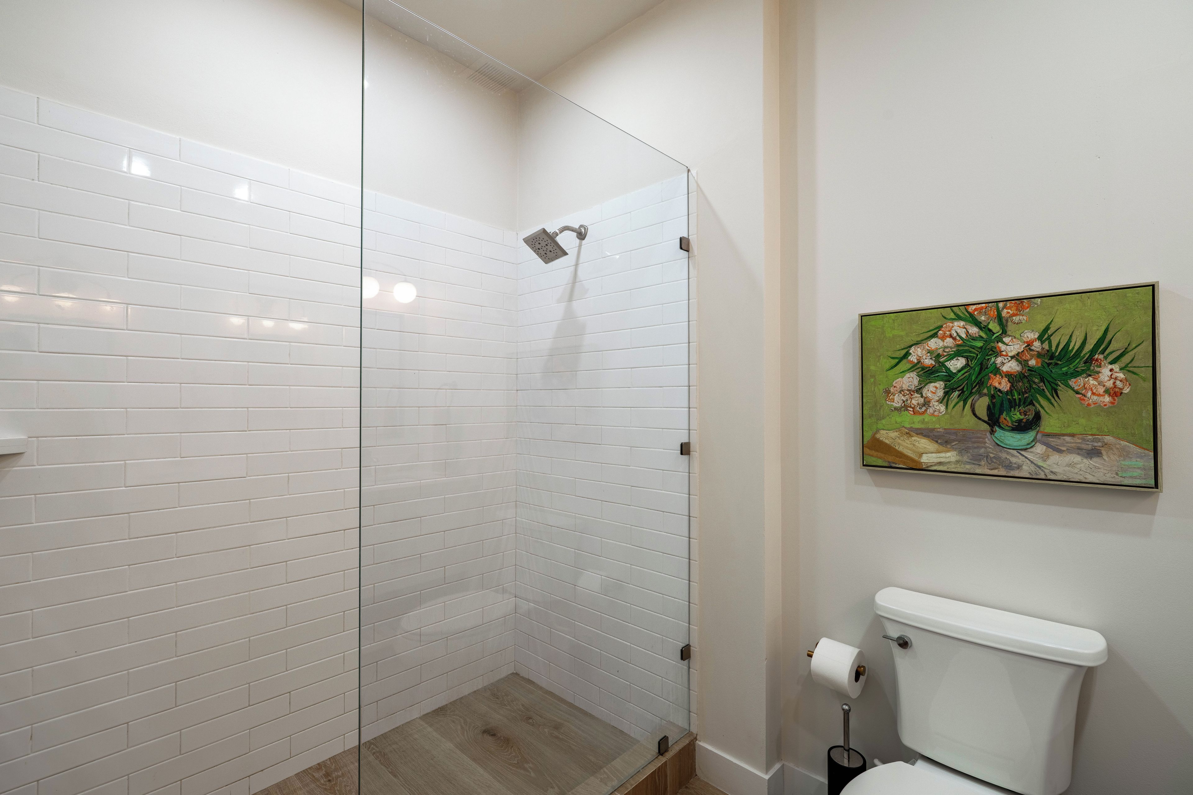 Ein Badezimmer mit Duschkabine aus Glas, Toilette und einem Bild an der Wand.
