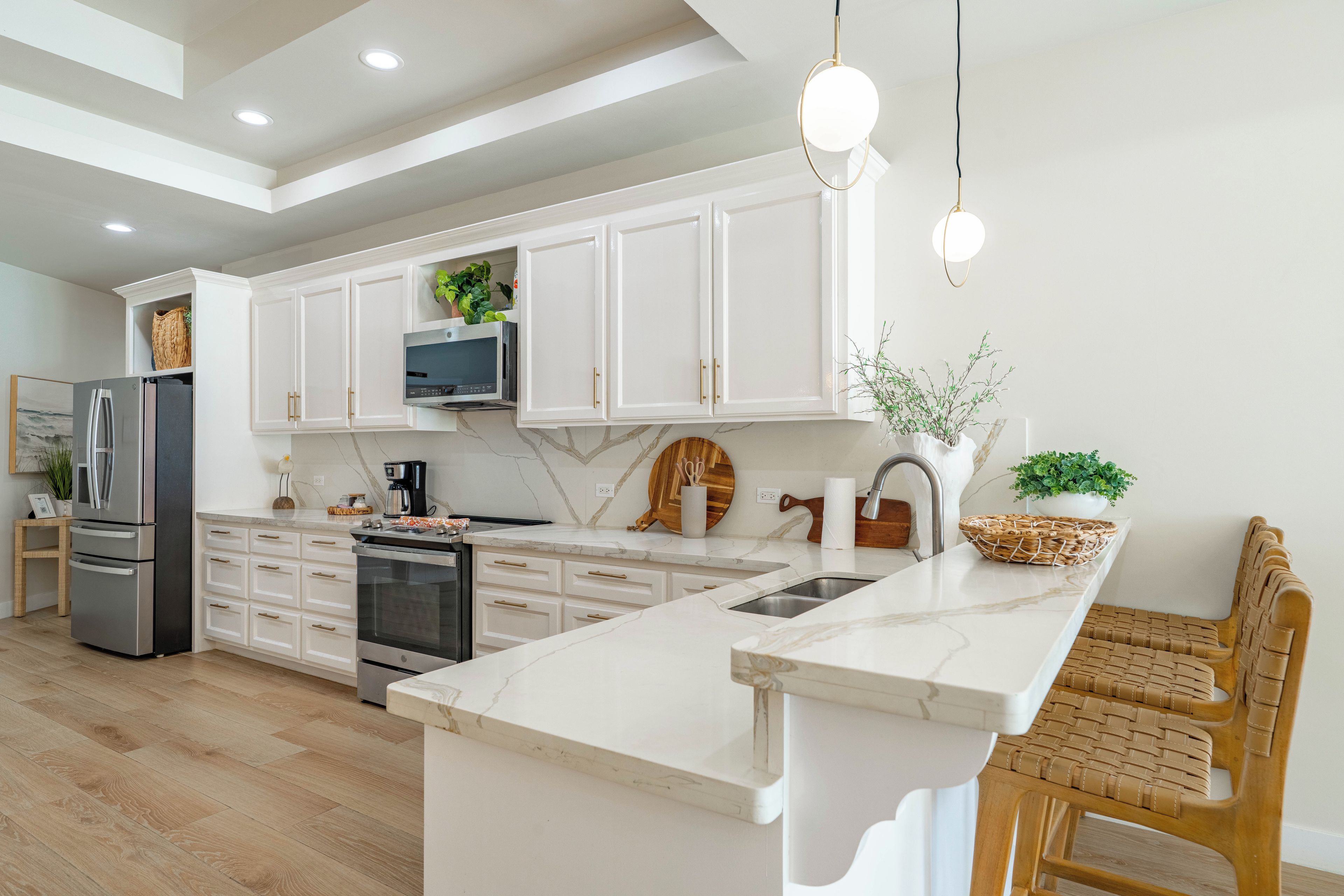 A modern kitchen with white cabinetry, a central island, stainless steel appliances, and a hanging light fixture.