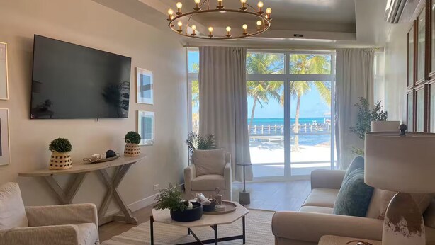 Una sala de estar moderna con un televisor grande, una araña y vista a la playa.