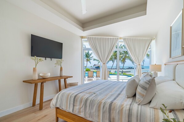 Un dormitorio con una cama, televisión, mesa de madera y vista al océano.