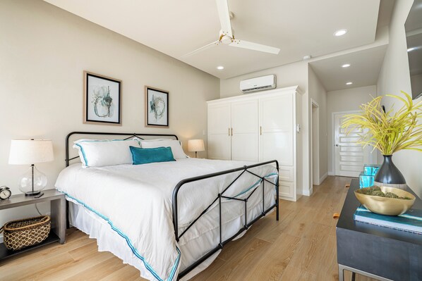 A bedroom with a bed, bedside tables, a ceiling fan, framed artwork, and a wardrobe. - Styles Beach 1D - Luxury Beachfront Condo w/ Pool (San Pedro)