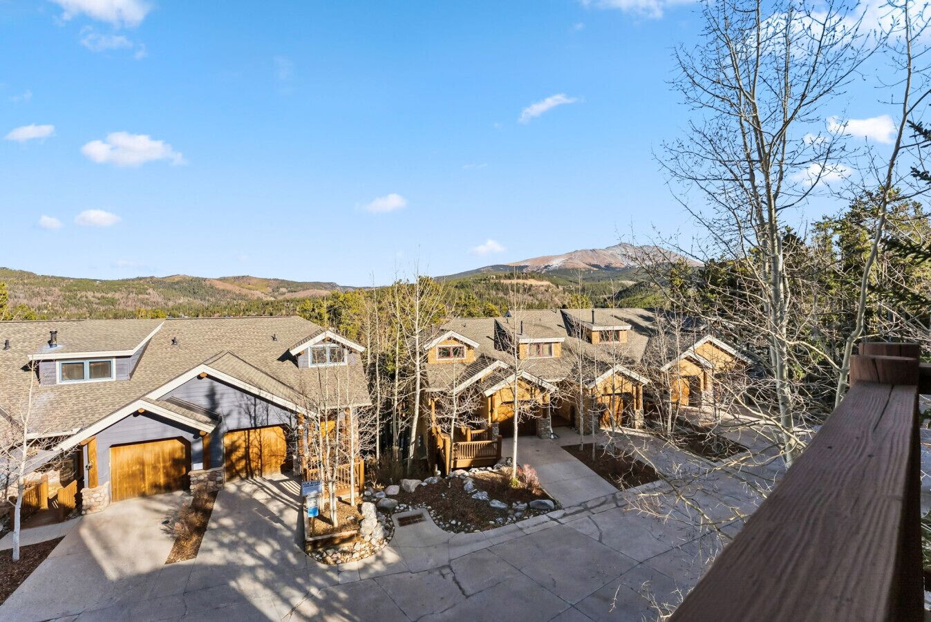 A row of houses with sloped roofs and wooden exteriors, set against a backdrop of hills and a clear sky.