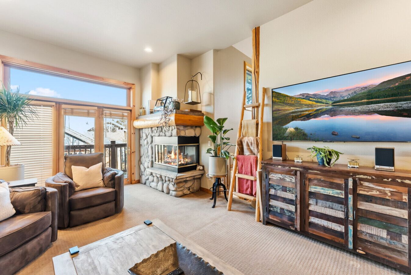 A cozy living room with a fireplace, a comfortable leather sofa, a television, and a scenic painting on the wall.